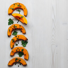 Delicious roasted pumpkin slices garnished with fresh herbs and black pepper on a white wooden surface