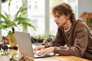 Creative young man focused on work at a sunny cafe surrounded by plants