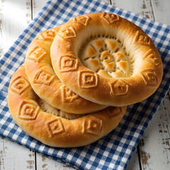 Golden brown round breads with decorative embossed patterns stacked on a blue and white gingham cloth