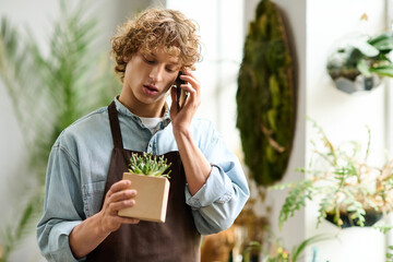Young creative man talks on the phone while holding a small plant in a vibrant space