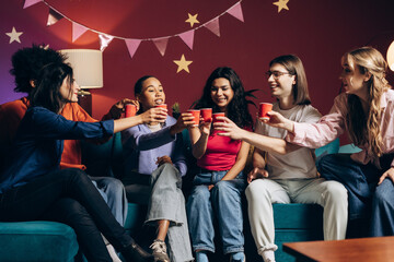 Fototapeta premium Diverse young friends celebrating and toasting with red cups at a fun house party