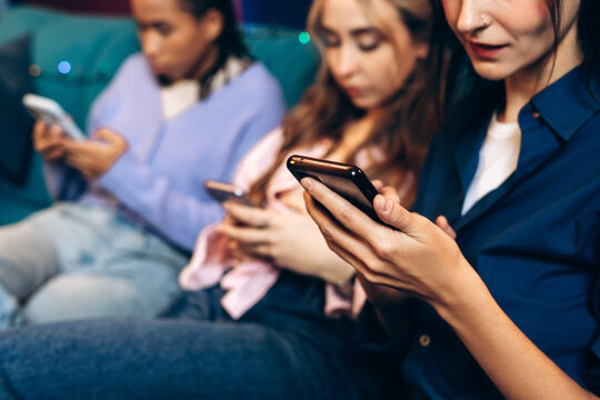 Young women ignoring friends at social gathering, busy using mobile phones