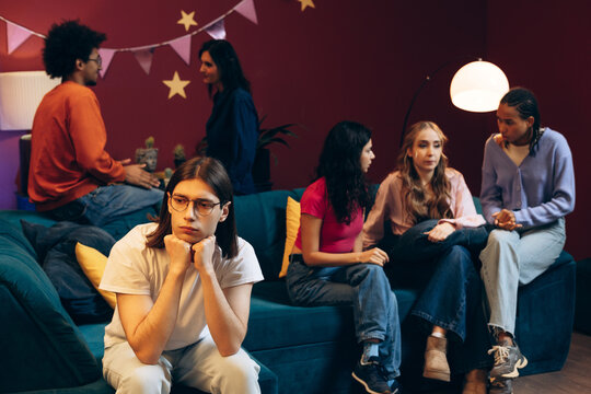 Young man feeling lonely at a party while friends socialize in the background