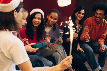 Friends celebrating Christmas party, exchanging gifts and holding sparklers, champagne flutes