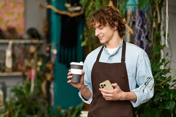 Young creative man enjoying coffee while checking his phone in a vibrant cafe setting