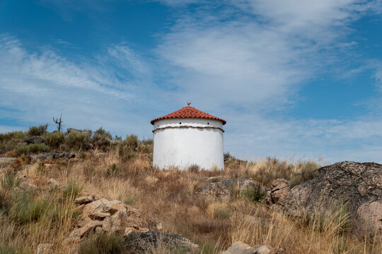 Pombal de arquitetura tradicional de paredes brancas e telhado de terracota numa colina &aacute;rida e rochosa sob um c&eacute;u azul no parque natural de Faia Brava em Portugal