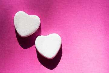 Two white heart shaped Valentine candies on pink background