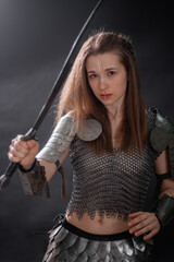 Obraz premium Portrait of a young woman, fantasy warrior in armor with a sword in her hands isolated on a dark background.