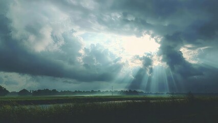 Sunbeams break through dark storm clouds over a flat rural landscape with fields and a river. Concept Dramatic Sky, Rural Landscape, Sunbeams, Storm Clouds, River and Fields