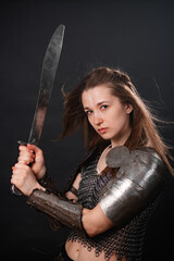 Obraz premium Portrait of a young woman, fantasy warrior in armor with a sword in her hands isolated on a dark background.