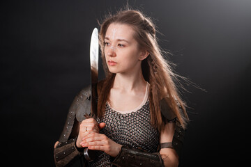 Obraz premium Portrait of a young woman, fantasy warrior in armor with a sword in her hands isolated on a dark background.