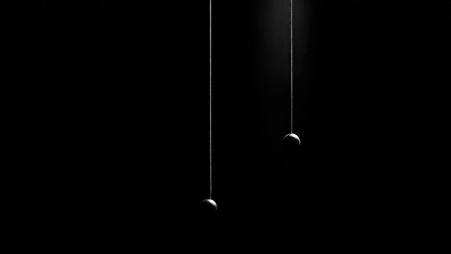 Two small spheres hang from thin strings against a black, minimalist background. Concept Minimalist Still Life, Floating Spheres, Thin Strings, Black Background, Geometric Composition