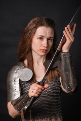 Obraz premium Portrait of a young woman, fantasy warrior in armor with a sword in her hands isolated on a dark background.