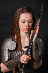 Obraz premium Portrait of a young woman, fantasy warrior in armor with a sword in her hands isolated on a dark background.