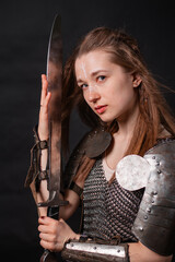 Obraz premium Portrait of a young woman, fantasy warrior in armor with a sword in her hands isolated on a dark background.