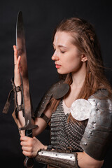 Obraz premium Portrait of a young woman, fantasy warrior in armor with a sword in her hands isolated on a dark background.
