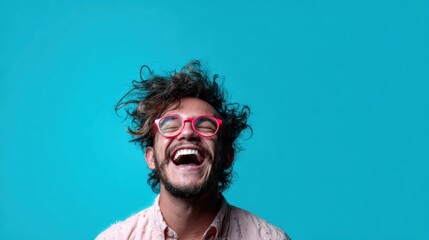A man with curly hair and glasses laughs joyfully, showcasing a charming expression against a vivid turquoise backdrop that radiates happiness and positivity.