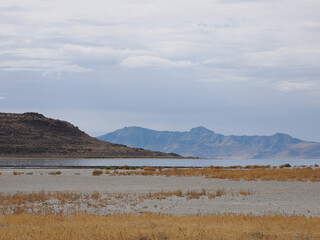 Barren salt flats and arid grass leading to Great Salt Lake and mountains