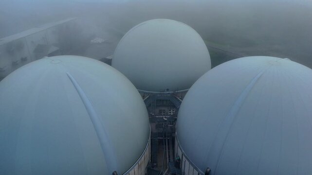 Aerial drone view of industrial factory domes, biogas generation production plant in foggy conditions with smoke stacks, Bury Saint Edmunds, UK