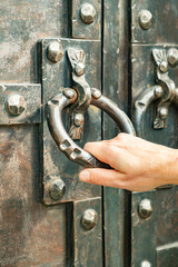 Large antique door handle is gripped by a hand, showcasing intricate metalwork and details