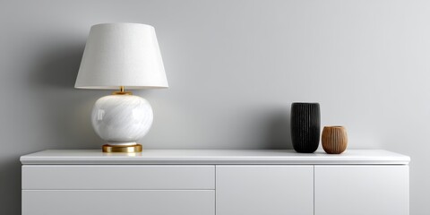 White modern lamp on a sleek white sideboard accompanied by black and wooden vases against a minimalist gray wall