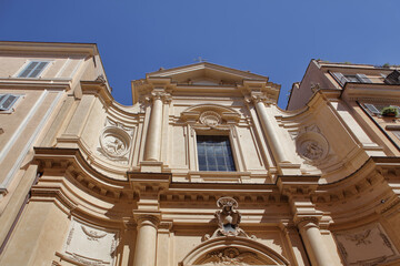 Baroque facade of the Church of Santa Caterina da Siena a Via Giulia in Rome, Italy. Curved lines, columns, and ornate carvings under a bright blue sky.