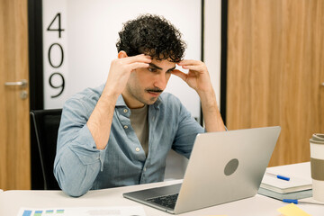 Young man experiencing stress analyzing data on laptop