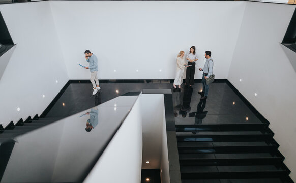 A group of coworkers gathers on a sleek open staircase in a bright, contemporary office lobby, sharing notes and devices as they discuss plans and collaborate.