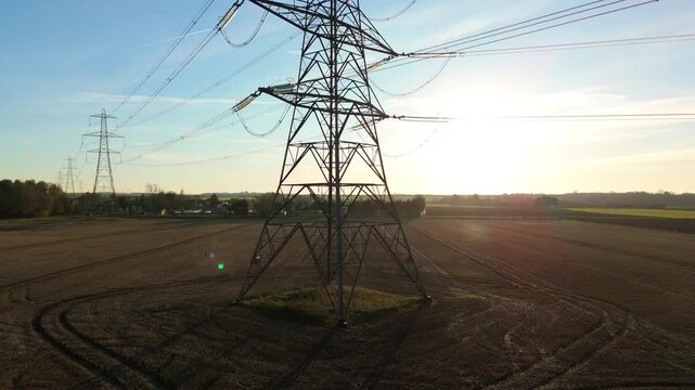 Aerial drone view cinematic shot of electricity cables powerlines and pylons silhouetted against sunset in winter, Energy infrastructure power plant, UK