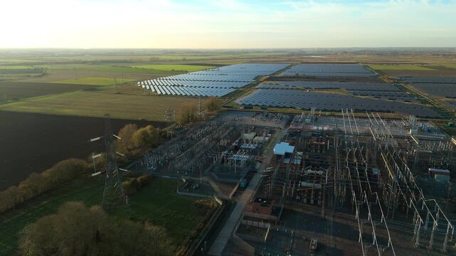 Drone aerial footage of electrical substation and photovoltaic solar energy source with transformers and pylons at sunset near Burwell Newmarket UK