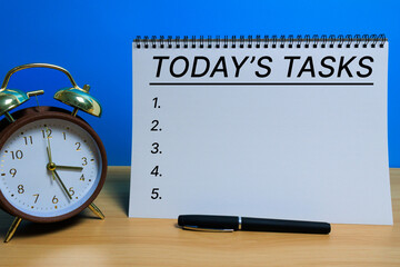 White spiral notebook with the text “Today’s Task” beside an alarm clock on a blue background, symbolizing the self-care concept of gentle planning, mindful routines, and calm daily intention setting.