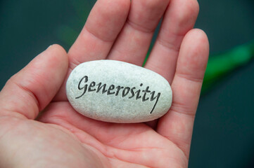 Hand holding a white stock with Generosity text engraved on it.