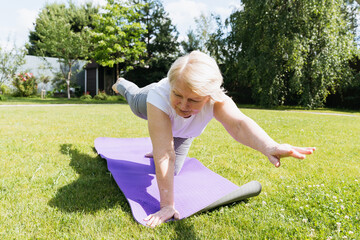 Active senior woman practicing yoga on mat in garden, smiling while exercising outdoors on a sunny day