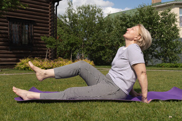 Senior woman exercising outdoors on a yoga mat in a sunny garden, stretching and enjoying an active healthy lifestyle. Relaxed expression and natural environment emphasize wellness and outdoor fitness