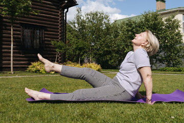 Senior woman exercising outdoors on a yoga mat in a sunny garden, stretching and enjoying an active healthy lifestyle. Relaxed expression and natural environment emphasize wellness and outdoor fitness