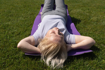 Elderly woman lying on a mat in the garden, relaxing with hands behind head on a sunny summer day