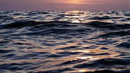 A serene ocean surface at sunset with gentle waves reflecting sunlight. Captured from a low angle, ideal for a calming video backdrop. Live desktop wallpaper.