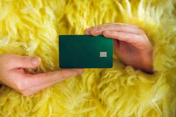 Hands holding a green credit card against a vibrant yellow fluffy background, showcasing financial...