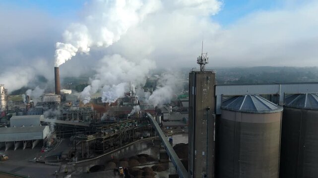 Aerial drone cinematic view of a large sugar factory showing silos chimney stacks smoke plumes and pollution in foggy winter Bury Saint Edmunds UK