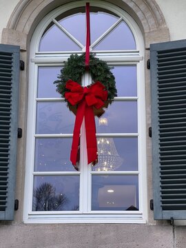 weihnachtliches Fenster gr&uuml;ner Kranz mit roter Schleife und wei&szlig;e Sprossenfenster, adventliche Stimmung