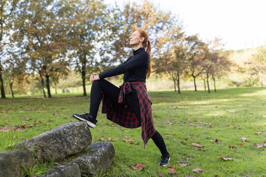 Woman stretching leg on stone in park