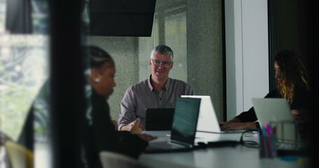 Coworkers quietly concentrate on laptop tasks during team meeting in bright office environment with natural daylight and modern collaborative setup