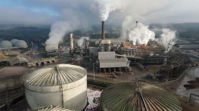 Aerial drone cinematic shot of industrial sugar production factory with silos chimney stacks smoke plumes in foggy winter Bury Saint Edmunds United Kingdom