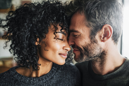 primer plano de una pareja de enamorados haci&eacute;ndose caranto&ntilde;as y d&aacute;ndose besos con fondo borroso de una casa luminosa