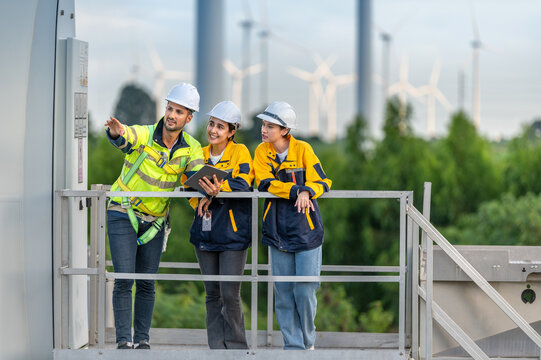 Team of Engineers Planning Project for Renewable Energy Professional Team Inspecting Wind Turbines for Clean Energy Generation Collaboration : Engineers with Blueprint at Wind Farm.