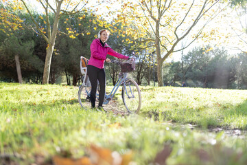 Woman pushing bicycle in autumn park listening to music