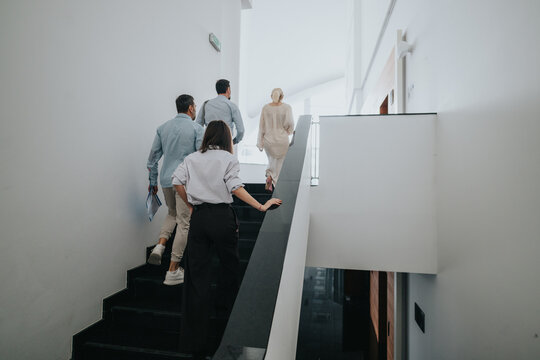 A diverse group of people climb a sleek staircase in a bright, minimal hallway. The scene conveys teamwork, progress, and a contemporary business atmosphere suitable for corporate and office imagery.