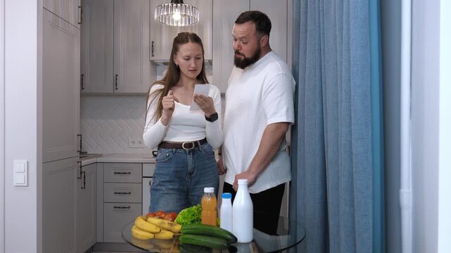 Happy couple unpacking groceries at home while checking receipt from store