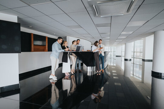 People gather around a modern bar in a bright atrium, exploring laptops and tablets, while colleagues discuss plans in a relaxed, businesslike setting. - Powered by Adobe