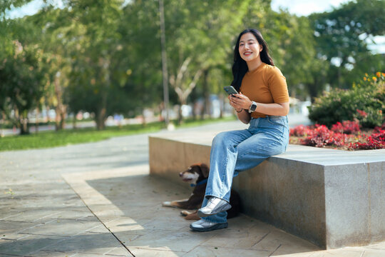 Woman with dog using smartphone sitting in park - Powered by Adobe